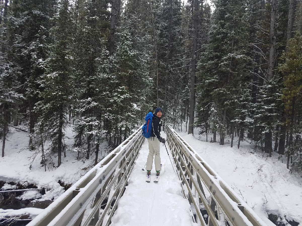 A skier with a backpack crosses a bridge heading into the backcountry.