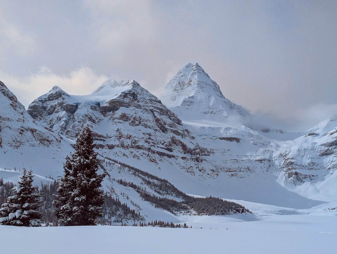 Snow-covered Mount Assiniboine dominates the sky line across frozen Lake Magog.